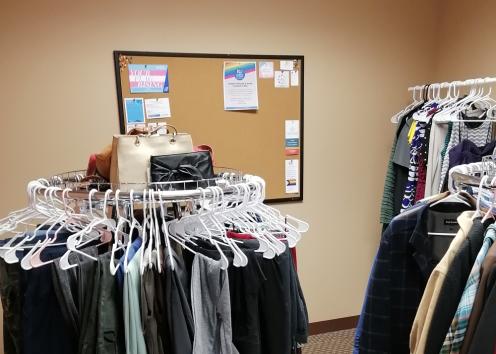 Three clothing racks with a bulletin board with resources