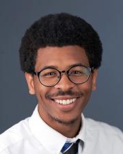 Photograph of Cornelius, wearing glasses, white button up, and blue tie