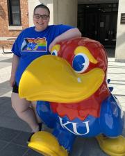 Photo of Program Coordinator Cori Deming leaning against a Jayhawk statue.